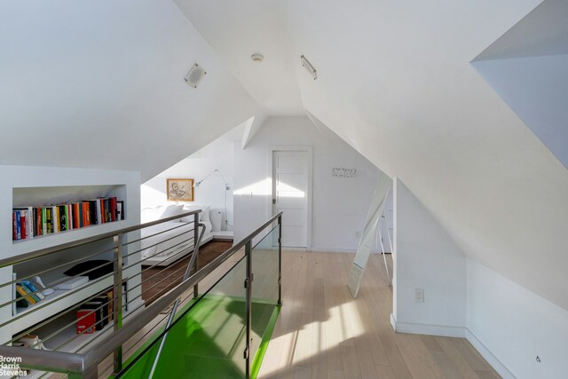 bonus room with built in shelves, lofted ceiling, and light wood finished floors