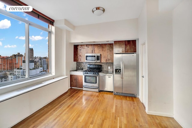 kitchen with a view of city, light wood finished floors, light countertops, decorative backsplash, and appliances with stainless steel finishes