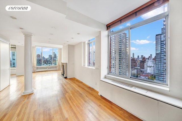 unfurnished room featuring a view of city, visible vents, light wood-style flooring, radiator heating unit, and ornate columns