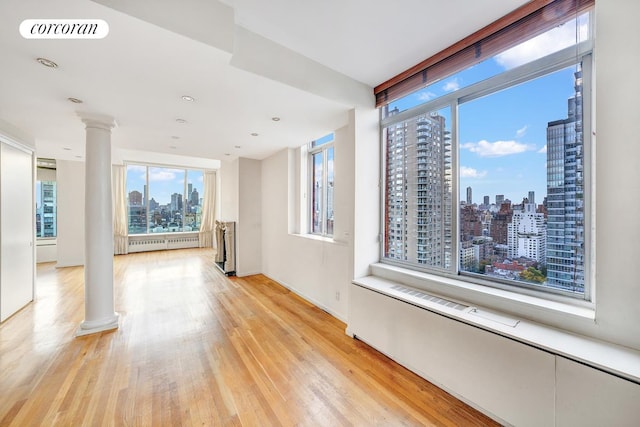 343 E 74th St Unit Ph34D, New York City, NY 10021 - empty room featuring decorative columns, a skyline view, light wood finished floors, and radiator heating unit