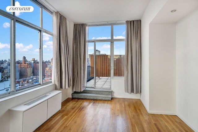 empty room with light wood finished floors, baseboards, and a city view