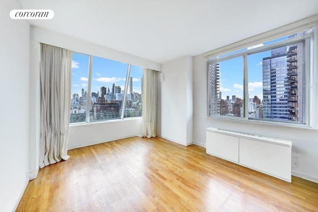 343 E 74th St Unit Ph34D, New York City, NY 10021 - spare room with a skyline view, light wood finished floors, radiator heating unit, and baseboards
