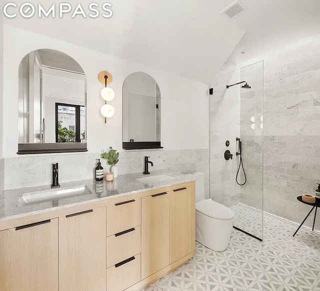 bathroom featuring a tile shower, lofted ceiling, tile walls, vanity, and toilet