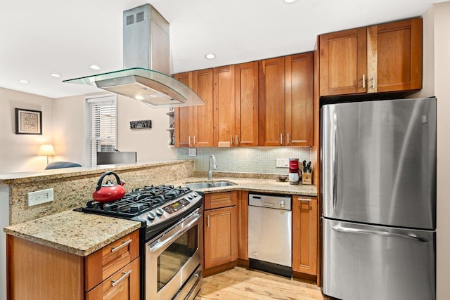 kitchen with island exhaust hood, appliances with stainless steel finishes, a sink, light stone countertops, and a peninsula