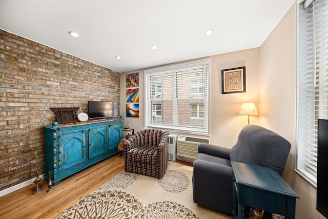 sitting room with light hardwood / wood-style floors, brick wall, and a wall mounted air conditioner