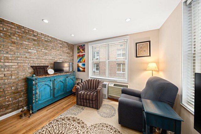 living area with an AC wall unit, brick wall, and light wood-type flooring