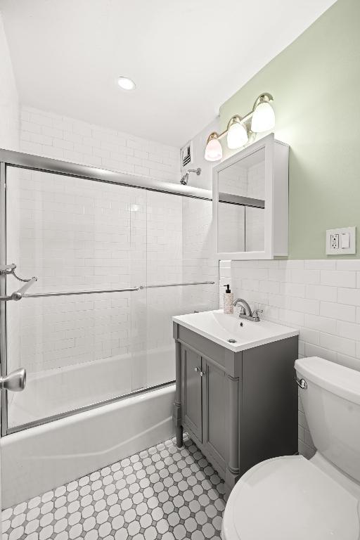 full bathroom with bath / shower combo with glass door, tile walls, toilet, and vanity