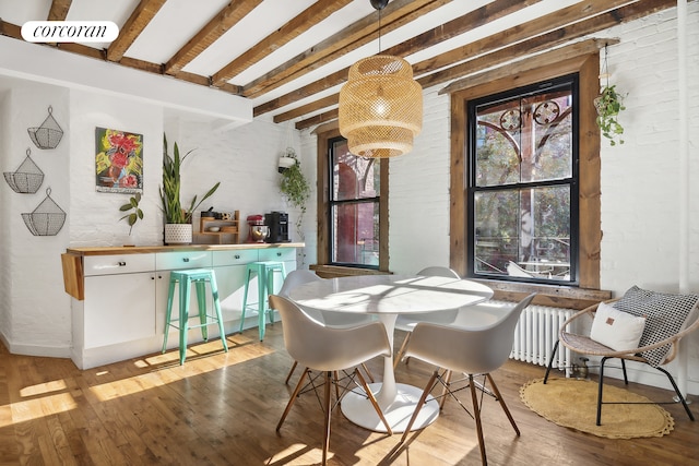 dining area with beamed ceiling, radiator, brick wall, and light wood-style floors