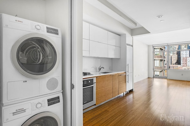 kitchen with black gas stovetop, dark wood-type flooring, white cabinetry, stacked washing maching and dryer, and stainless steel oven