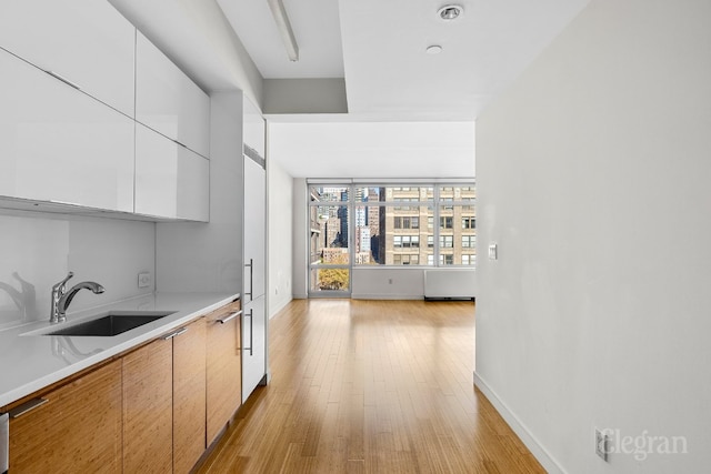 kitchen with light wood-type flooring, sink, and white cabinetry