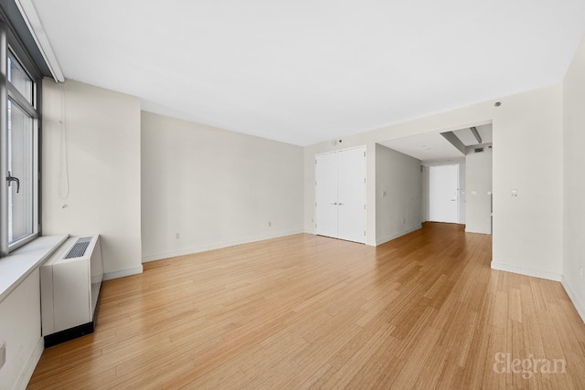 unfurnished living room with light wood-type flooring, plenty of natural light, and radiator heating unit