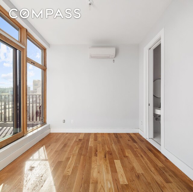 empty room featuring a wall mounted air conditioner, baseboards, and light wood-style floors