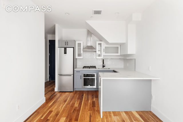 kitchen featuring visible vents, light countertops, decorative backsplash, stainless steel appliances, and wall chimney exhaust hood