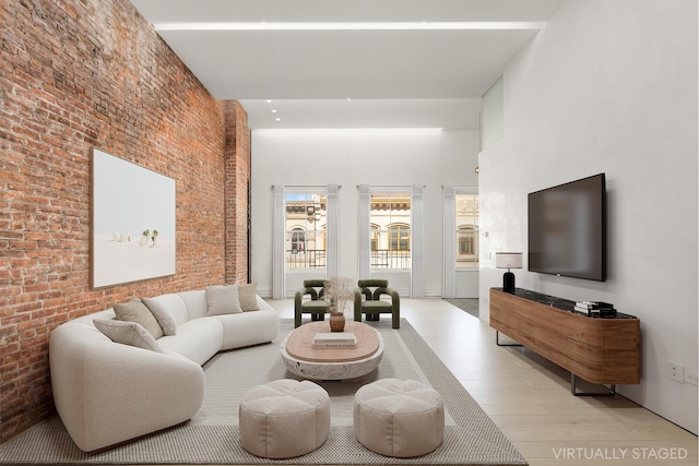 living room with a towering ceiling, brick wall, and light wood-type flooring