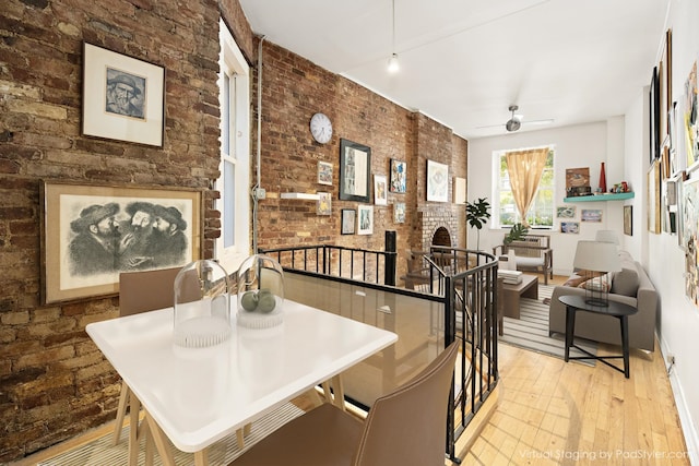 dining room featuring brick wall, a fireplace, a ceiling fan, and wood finished floors