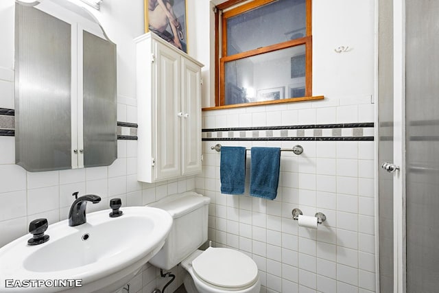 bathroom with toilet, sink, and tile walls