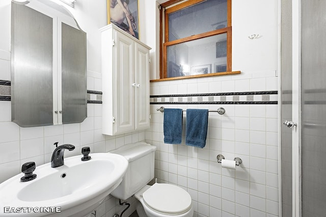 bathroom featuring a sink, tile walls, and toilet