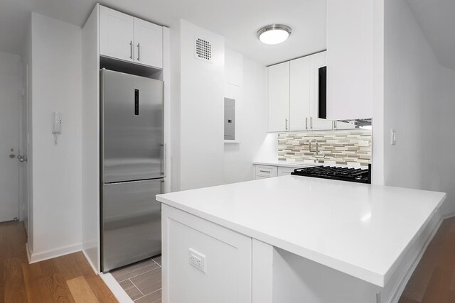 kitchen featuring kitchen peninsula, built in refrigerator, backsplash, light wood-type flooring, and white cabinets