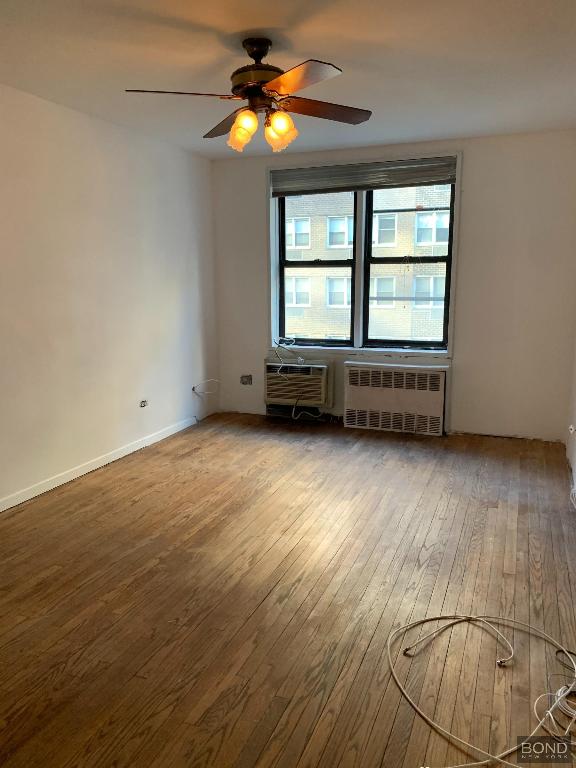 empty room with ceiling fan, a wall mounted AC, radiator, and hardwood / wood-style floors