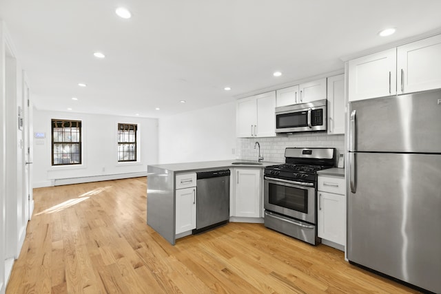 kitchen featuring appliances with stainless steel finishes, a peninsula, baseboard heating, light wood-style floors, and a sink