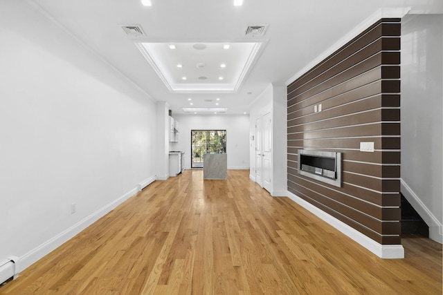 unfurnished living room with light wood finished floors, a baseboard radiator, a fireplace, and a raised ceiling