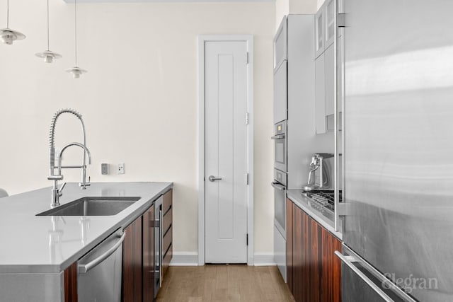 kitchen with decorative light fixtures, sink, appliances with stainless steel finishes, and light hardwood / wood-style flooring