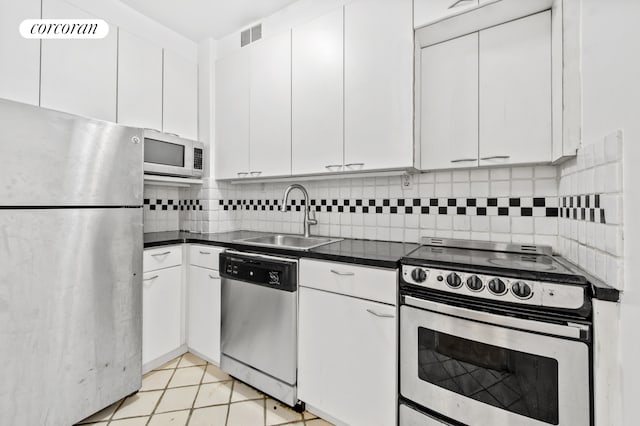 kitchen featuring appliances with stainless steel finishes, dark countertops, white cabinets, and a sink