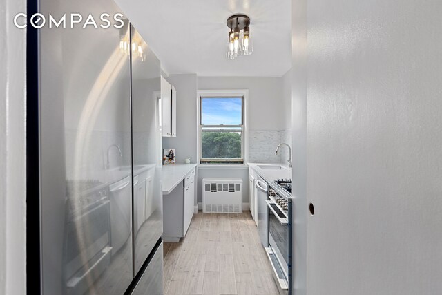 kitchen featuring light hardwood / wood-style floors, sink, white cabinetry, radiator, and appliances with stainless steel finishes