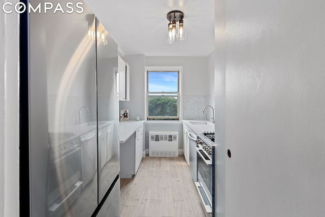 kitchen with appliances with stainless steel finishes, radiator heating unit, sink, white cabinets, and backsplash