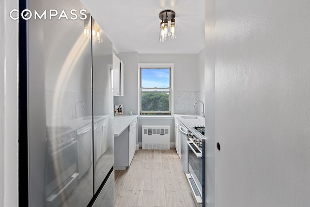 kitchen with stainless steel appliances, a sink, light countertops, backsplash, and radiator