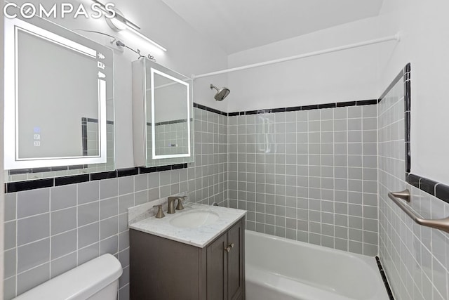 full bathroom featuring toilet, tiled shower / bath, tile walls, and vanity