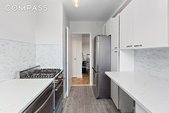 kitchen featuring light parquet floors, appliances with stainless steel finishes, white cabinetry, backsplash, and light stone countertops