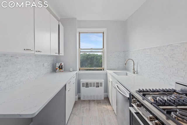 kitchen with sink, white cabinetry, light stone counters, radiator, and stainless steel appliances