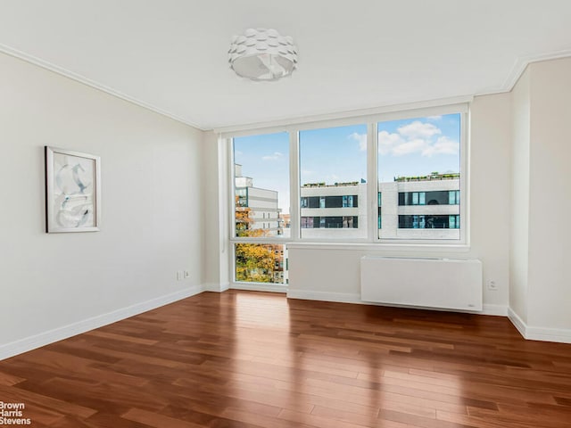 spare room with radiator, baseboards, wood finished floors, and ornamental molding