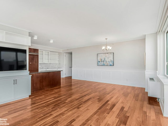 unfurnished living room featuring crown molding, light wood-style flooring, radiator heating unit, wainscoting, and a chandelier