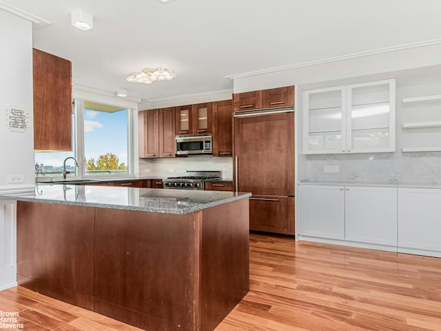 kitchen with gas range oven, stainless steel microwave, a sink, dark stone countertops, and paneled built in refrigerator