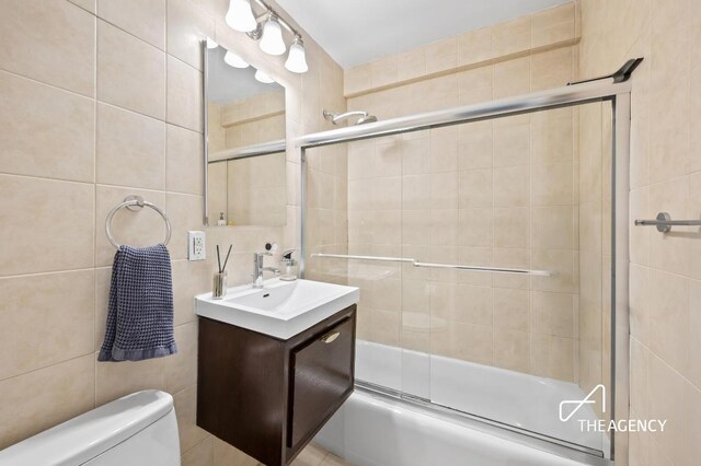 full bathroom with toilet, enclosed tub / shower combo, tile walls, and vanity