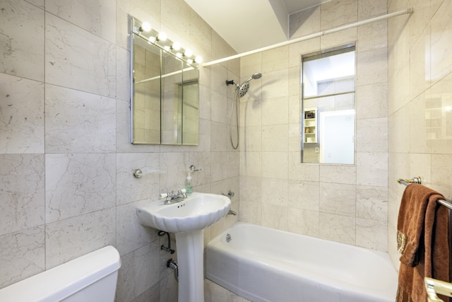 bathroom with tile walls, tiled shower / bath combo, and toilet