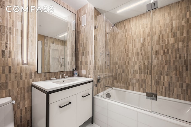 bathroom with shower / bath combination with glass door, tile walls, toilet, and vanity