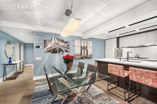 dining area featuring beamed ceiling, sink, and light hardwood / wood-style floors