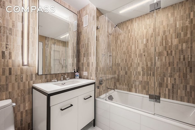 full bathroom with bath / shower combo with glass door, tile walls, vanity, and toilet