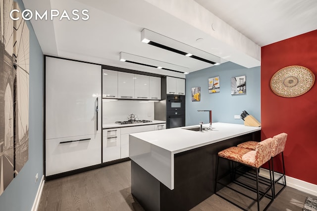 kitchen with a breakfast bar, stainless steel gas cooktop, white cabinetry, a sink, and wood finished floors