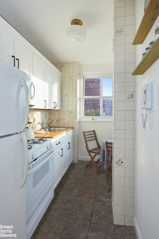 kitchen with tasteful backsplash, wooden counters, white cabinets, a sink, and white appliances