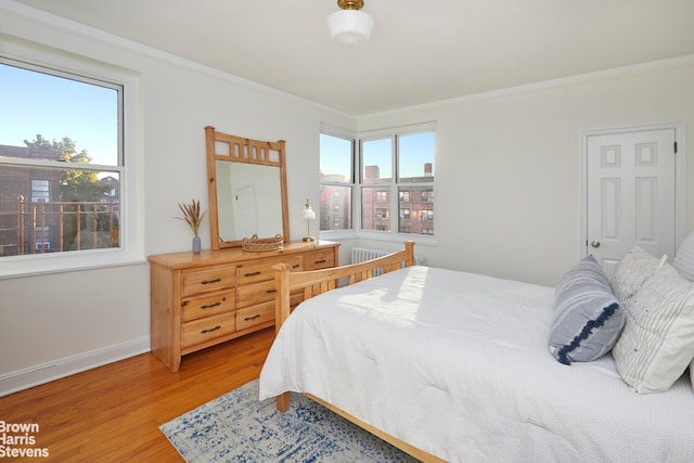 bedroom with multiple windows, wood finished floors, ornamental molding, and baseboards