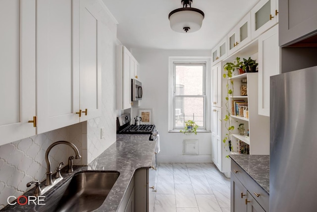 kitchen with white cabinetry, appliances with stainless steel finishes, sink, and dark stone counters