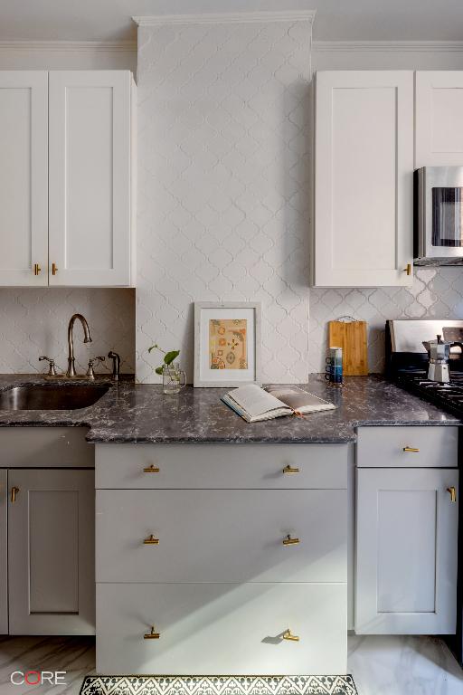 kitchen with sink, dark stone countertops, white cabinets, backsplash, and range