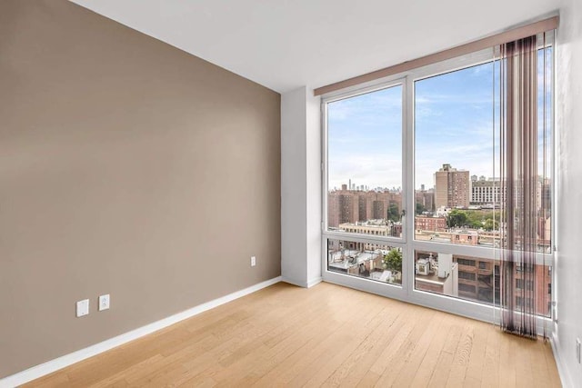 unfurnished room featuring floor to ceiling windows, a view of city, wood finished floors, and baseboards