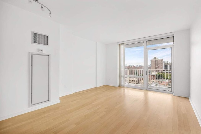 spare room featuring expansive windows, track lighting, and light hardwood / wood-style floors