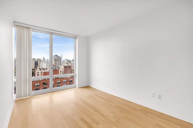 spare room with light wood-type flooring, baseboards, a city view, and floor to ceiling windows