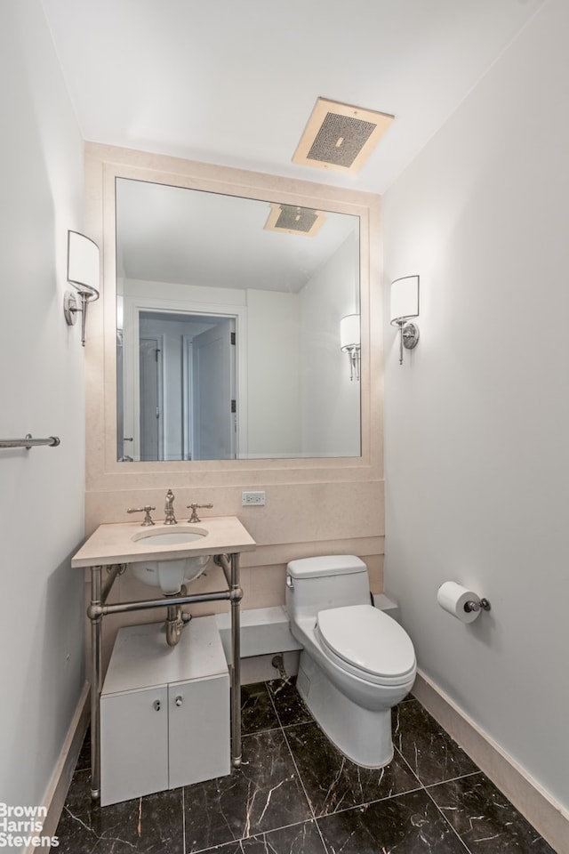 half bath featuring marble finish floor, baseboards, vanity, and toilet